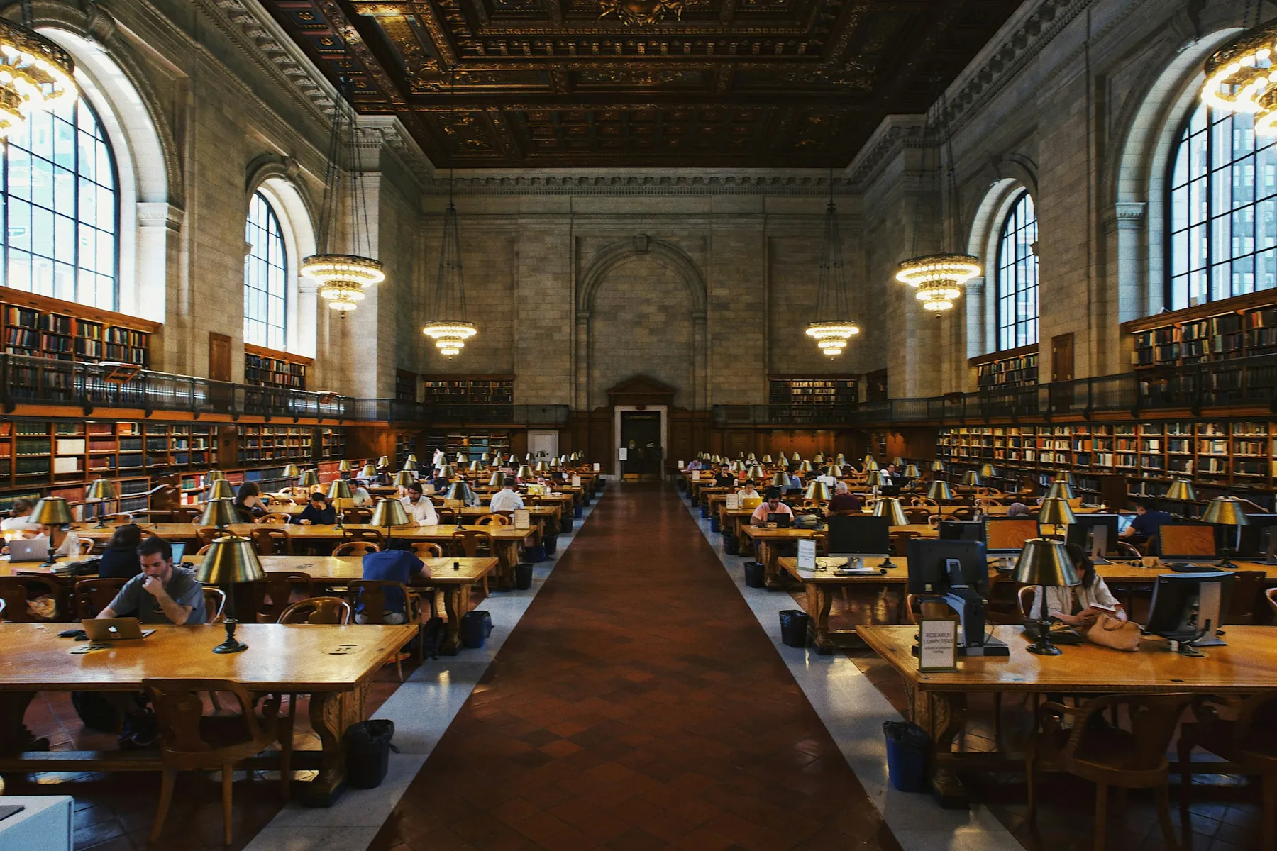 Long reading tables beneath arched windows in a public library